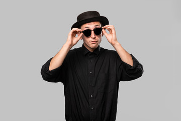 Portrait of a man in a black shirt, pork pie and sun glasses hat isolated over grey background.