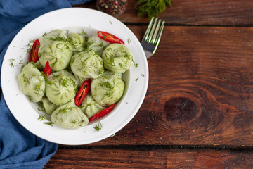 Boiled khinkali made of dough with spinach. Garnished with Red Chilli, Dill and Parsley. On a wooden background.