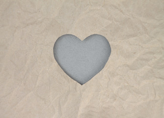 Fototapeta premium Gray felt heart on craft paper. Crumpled paper texture. Valentine's day stock photo for web, print and wallpaper. With empty space for text.