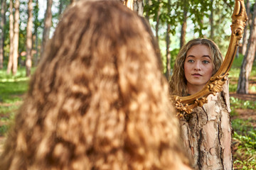 Back view of young woman watching her mirror image in a forest