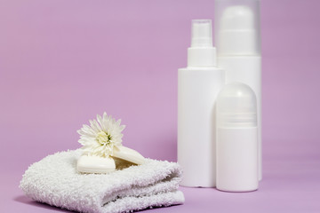 White bathroom accessories on a purple background. Products for hygiene. Soap, facial foam, tonic, deodorant, cotton towel. 