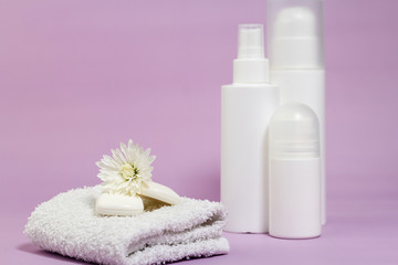 Obraz na płótnie Canvas White bathroom accessories on a purple background. Products for hygiene. Soap, facial foam, tonic, deodorant, cotton towel. 