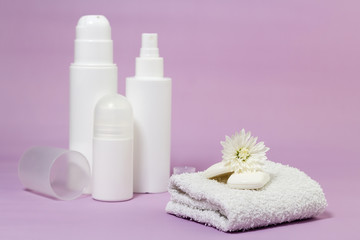 Obraz na płótnie Canvas White bathroom accessories on a purple background. Products for hygiene. Soap, facial foam, tonic, deodorant, cotton towel. 