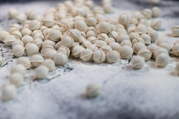 Flour pours onto the table. In order to make dough products, mini-dumplings are not stuck. Dumplings fall into flour. Dark marbled background.