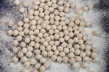 Flour pours onto the table. In order to make dough products, mini-dumplings are not stuck. Dumplings fall into flour. Dark marbled background.