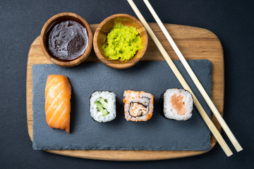 Top view of sushi rolls, maki, uramaki, nigiri and sashimi set served on stone slate.
