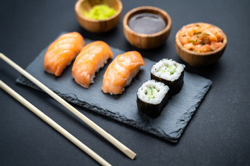 Top view of sushi rolls, maki, uramaki, nigiri and sashimi set served on stone slate.