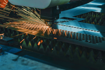 Machine for laser cutting of metal. Laser head cuts the sheet with a beam, sparks scatter