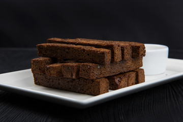 Crackers with garlic from black bread in oil on a wooden black background.