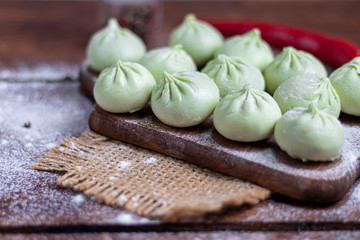 Frozen dough khinkali with spinach. Garnished with Red Chilli, Dill and Parsley. On a wooden background.