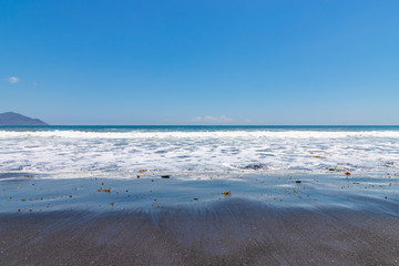 Blue Stones beach with black sand and ocean foam near Ende town, Flores Island, Indonesia