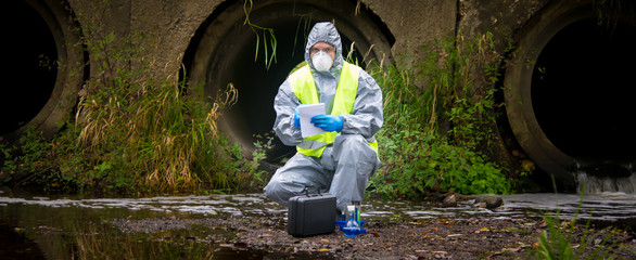 the scientist, wearing a protective suit, gloves and mask, took the liquid from the river, in test...