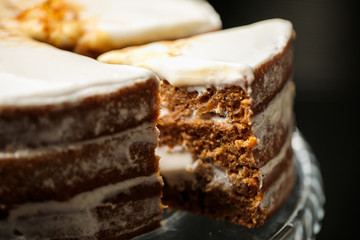 The slab of carrot cake (slice) with white cream on a glass tray. Black background.
