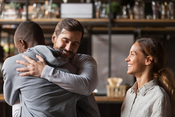Overjoyed diverse friends embrace welcoming pal in bar