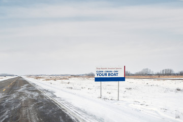 An advertisement reminding you to clean, drain and dry your boat along a deserted highway in a blustery prairie winter landscape