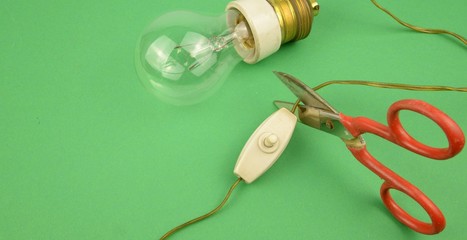 Ambiente, taglio degli sprechi energetici: forbici che tagliano il cavo di alimentazione di una vecchia lampadina a bulbo dotata porta lampada con isolante in ceramica, cavo e vecchio interruttore 