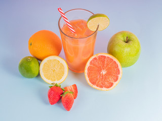 glass filled with natural fruit juice and surrounded by fruits on blue background. Oranges, strawberries, lemons, grapefruit surrounding the glass with juice