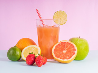 glass filled with natural fruit juice and surrounded by fruits on colored background. Oranges, strawberries, lemons, grapefruit surrounding the glass with juice