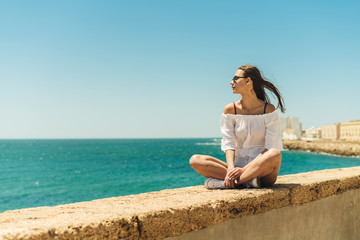 Fototapeta na wymiar beautiful sea shore, a girl sits on the parapet in lotus position and looks into the sea distance