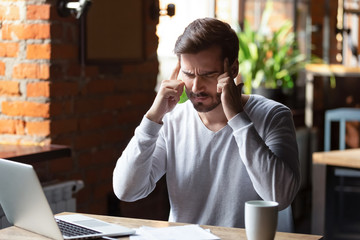 Tired man suffering from headache working at laptop in cafe