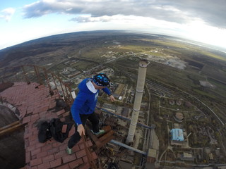 Man without any safety equipment walking on a thin rusted rail on top of a high abandoned stack...