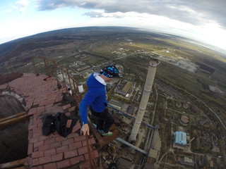 Man without any safety equipment walking on a thin rusted rail on top of a high abandoned stack...