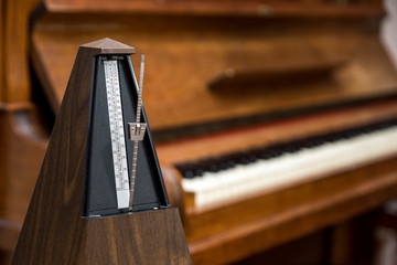 altes, analoges Metronom,  vor altem Piano, Klavier im Hintergrund. Selektive Schärfe