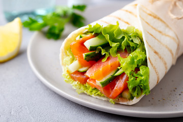 Fototapeta na wymiar Wrap sandwich, roll with fish salmon and vegetables. Grey background. Close up.