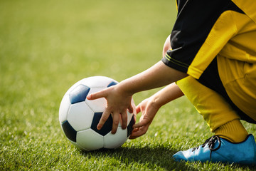 Child playing with soccer ball on grass venue. Little kid holding in both hands football ball. Young soccer player in blue cleats
