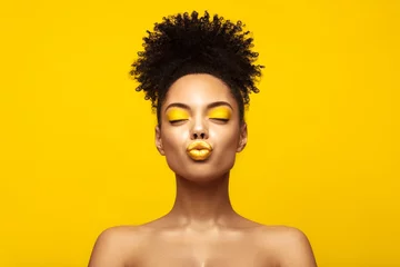 Foto auf Acrylglas Enjoyed African American Fashion Model portrait . Satisfied Brunette young woman with afro hair style and closed eyes show kiss,creative yellow make up, lips and eyeshadows on colorful background. © Beauty Agent Studio