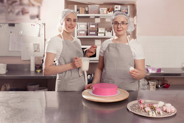 two women in the professional kitchen are going to decor one cake with cream