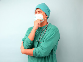 male asia surgeon,surgeon showing stethoscope wearing surgeon mask, on a blue background in studio.