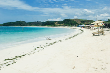 Sea view from tropical beach with sunny sky. Beach chairs on the white sand beach with cloudy blue sky. Seascape with huge waves at beautiful hidden white sand. Summer holidays at ocean beach. 
