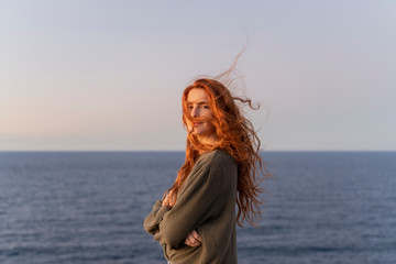 Fototapeta na wymiar Portrait of redheaded young woman with windswept hair at the coast at sunset, Ibiza, Spain