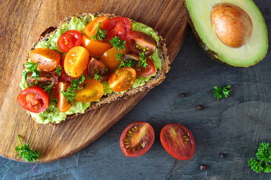 Healthy avocado toast with cherry tomatoes. Close up table scene over a dark background.