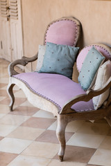 Pink textile vintage style sofa with blue and gray pillows near peachy background. Interior concept.