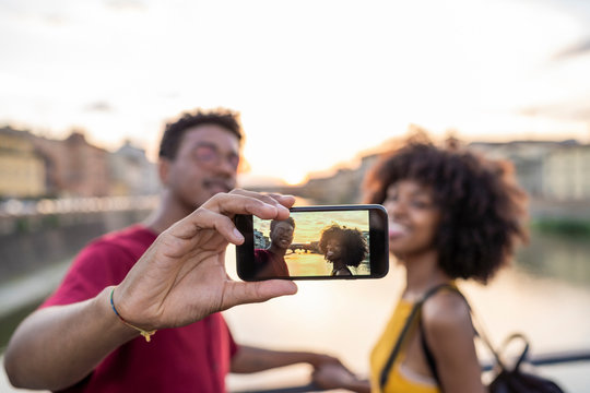 Young tourist couple taking a selfie on a bridge above river Arno at sunset, Florence, Italy