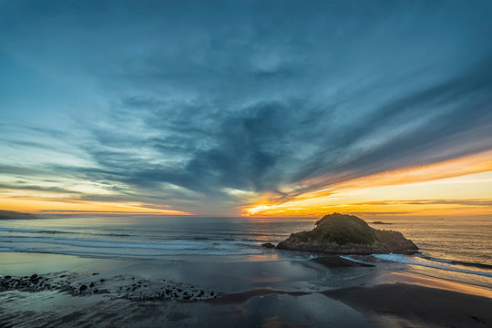 New Zealand, Tongaporutu, Cloudy sky over sandy coastal beach at sunset with Motuotamatea island in background
