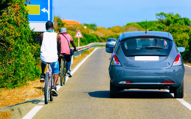 Bicycles and car on road at in Sardinia Island in Italy in summer. Bikers driving scooter on...