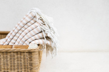 White stripe cotton bath towels lying in whicker basket on white background. Organic pestemal towels made of natural eco materials.