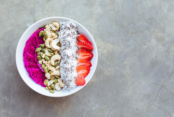 Healthy breakfast smoothie bowl topped with pitaya, cashew, coconut flakes and strawberry on gray background. Copy space.