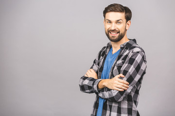 Happy young man. Portrait of handsome young man in casual keeping arms crossed and smiling while standing against grey background.