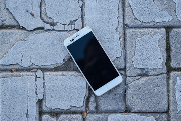Broken cell phone on an old cobblestone floor. Concept of technology.