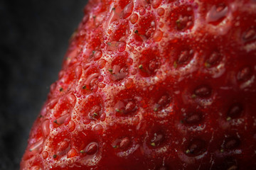 A close up super macro photograph of a freshly washed ripe organic strawberry covered in water droplets