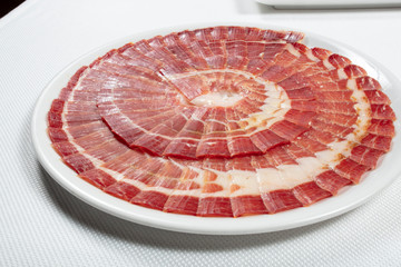 jamón iberico de bellota cortado en plato sobre fondo blanco. Iberico de bellota ham sliced ​​on a plate on a white background.