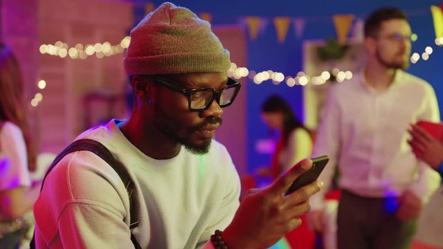 Young attractive african man in fashion outfit chatting onlne on smartphone using application staying at party for best friends. People and nomophobia concept.