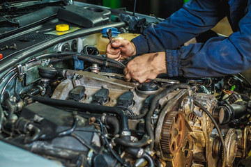 Close up hands of unrecognizable mechanic doing car service and maintenance. Cropped image of handsome young auto mechanic in uniform repairing car in auto service.