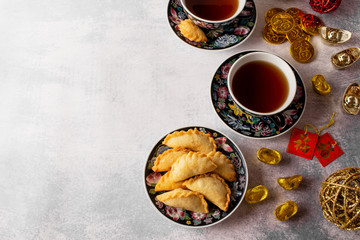 Chinese symbols on ornaments, red pockets and coins, means wealth. Tea setting with deep fried puff pockets, yau gok. Traditional Chinese New Year snack eating during celebration season.