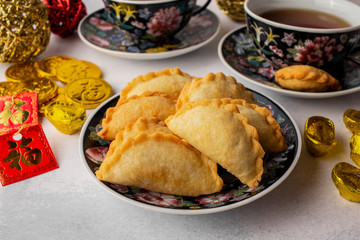 Chinese symbols on ornaments, red pockets and coins, means wealth. Tea setting with deep fried puff pockets, yau gok. Traditional Chinese New Year snack eating during celebration season.
