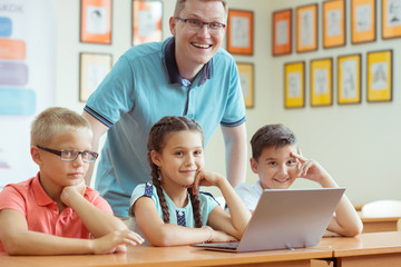 Young handsome teacher with group of clever children working with laptop during a lesson